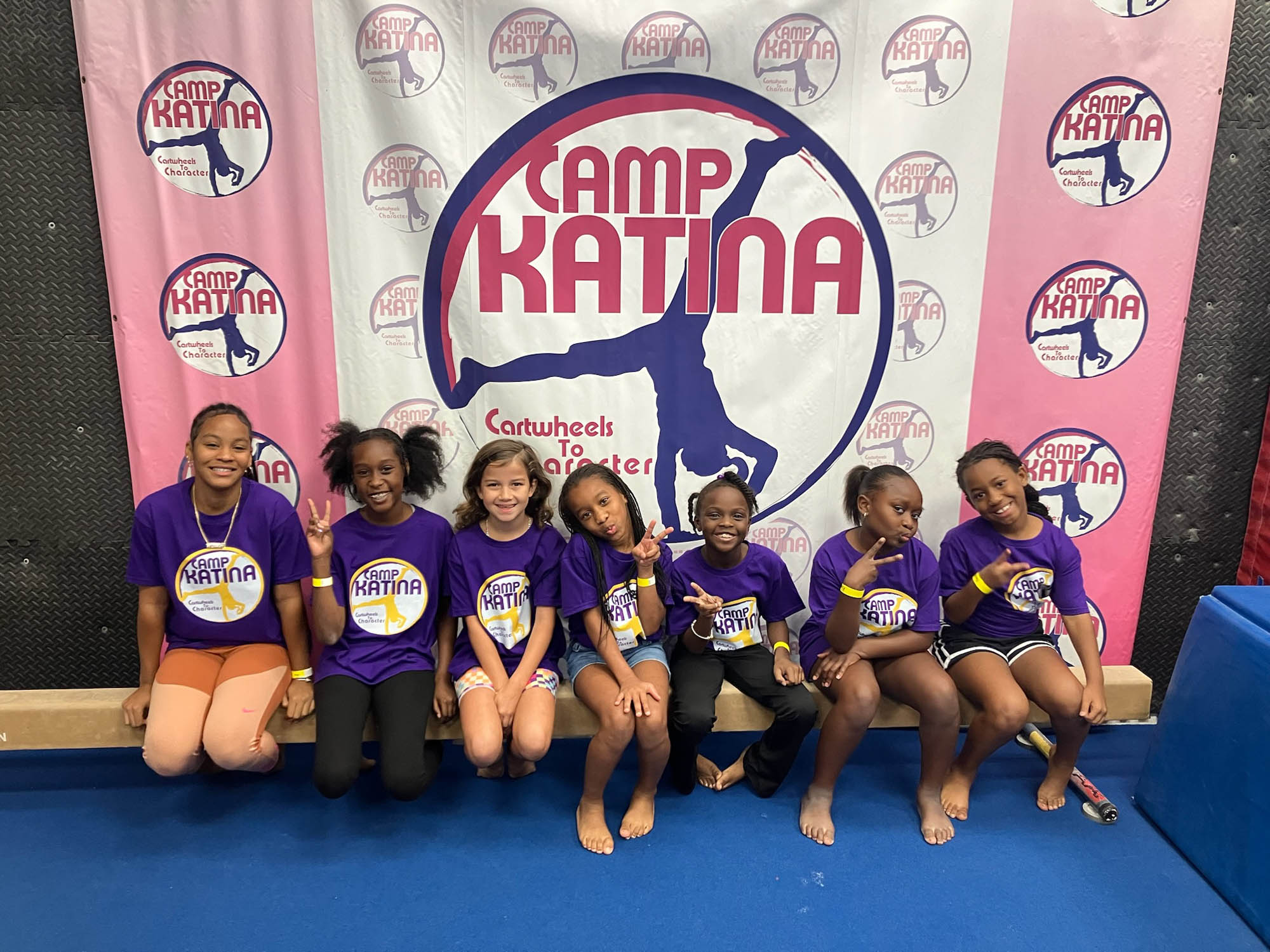 a group of young girls sits in front of a Camp Katina sign