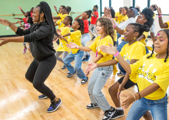a woman leads a group of girls in a dance routine in a dance studio