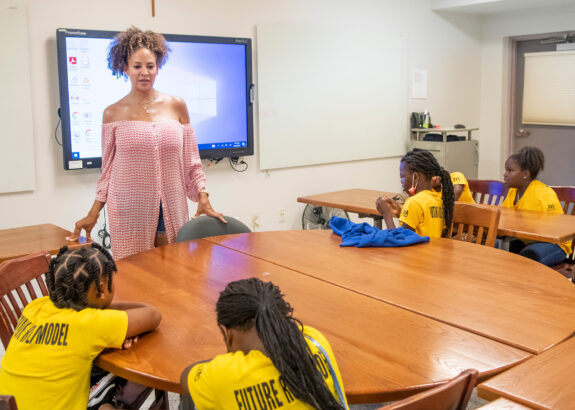 Tracy Wilson Mourning speaks to a group of girls seated around a table in a classroom